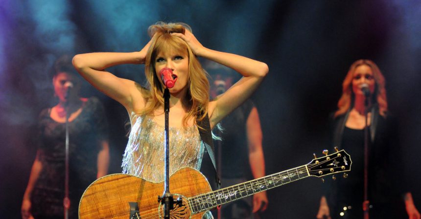 Taylor Swift holds her head in her hands on stage