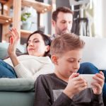 Family ignoring each other in lounge room while using screen devices