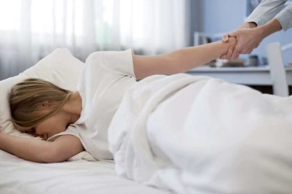 A mother's hand tries to pull a sleeping teenager from her bed.