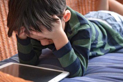 Boy lays on couch with head in hands while using iPad