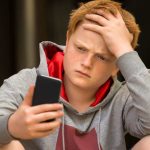 Teenage boy looks sad using his phone