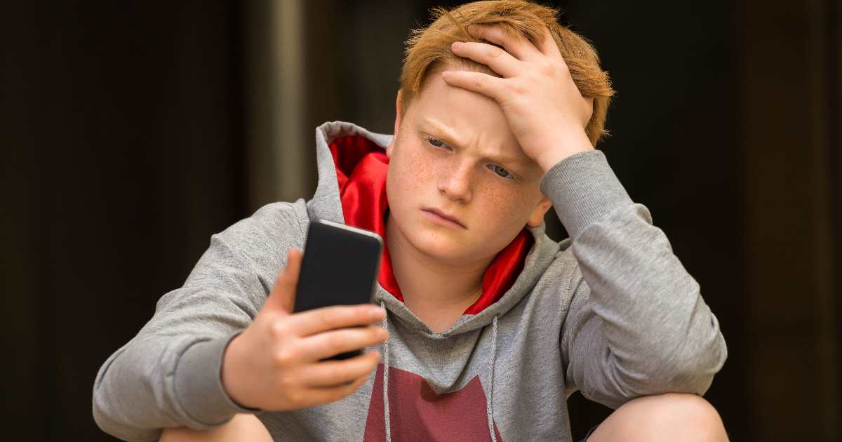 Teenage boy looks sad using his phone