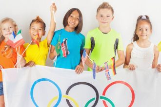 Young kids celebrate the Olympics holding a large Olympic ring flag